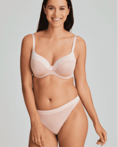 Brunette woman smiling at the camera whilst stood wearing the Prima Donna Twist Glow Lingerie Set in Powder Rose Glow